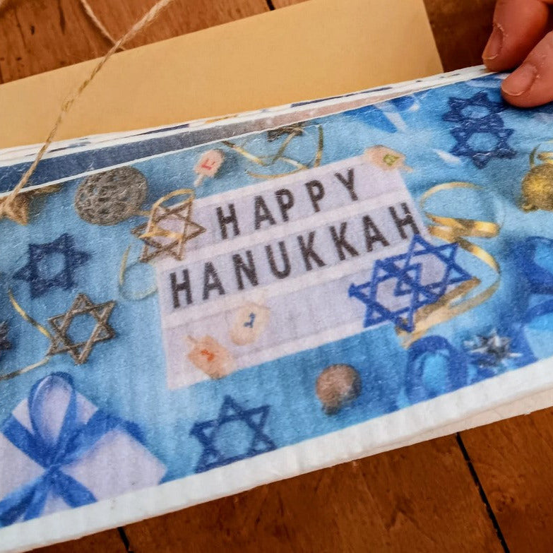 Happy Hanukkah Swedish Dish Cloth Holiday Card – eco-friendly reusable greeting card by Earthly Change featuring blue festive design with Star of David, dreidels, and gifts.