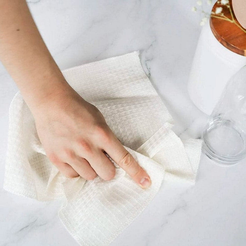 Hand using a white cloth on a marble surface with a glass and plate in the background