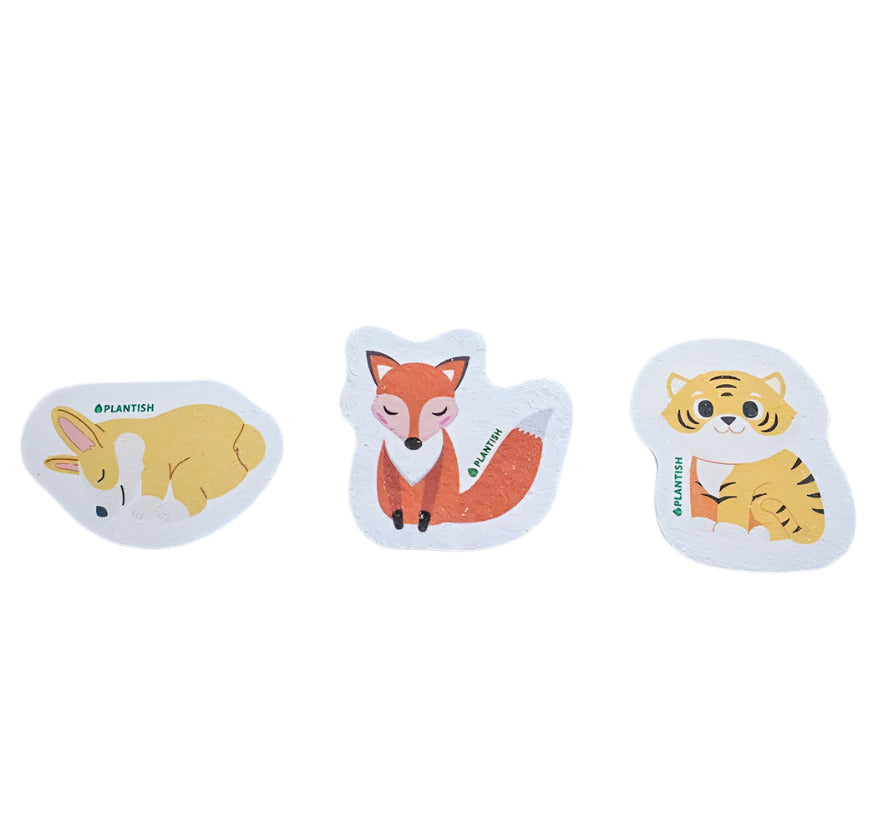 Three animal-shaped pop-up sponges on a dark surface, with designs resembling a dog, fox, and tiger, respectively.