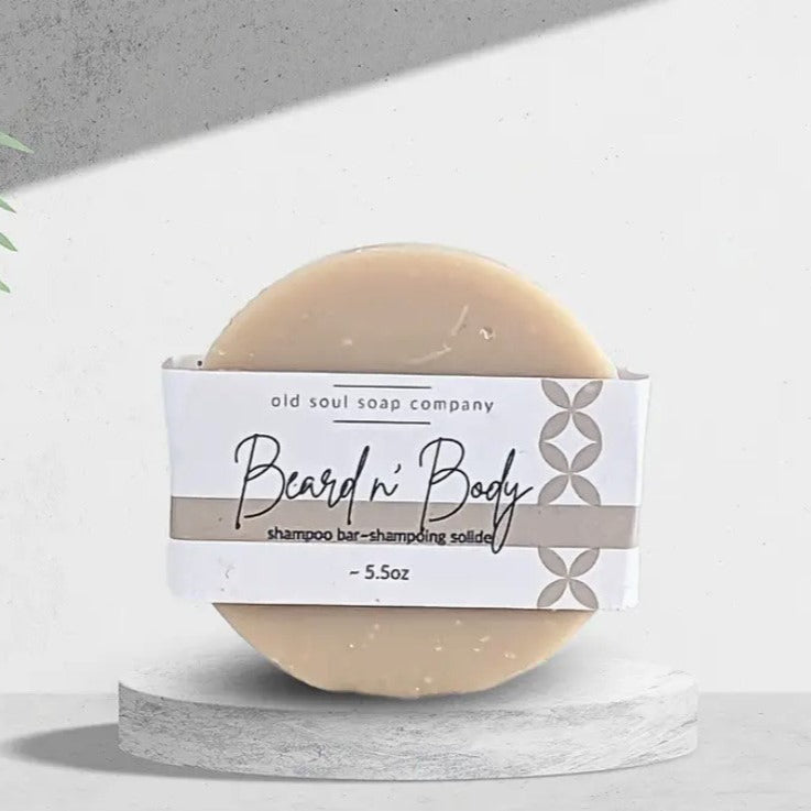 Labelled round Old Soul Soap Company Beard n' Body 5.5 oz handcrafted shampoo bar standing on its side on a white background.