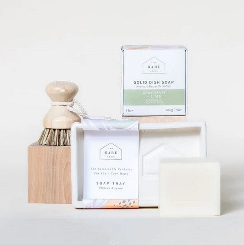 This Bare Home kitchen gift set is shown on a white background and includes a white handmade pottery soap tray with a white matte glaze, a bergamot lime solid dish soap cube and a durable pot scrubber.