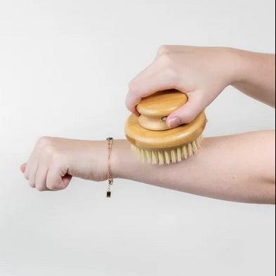 Round bamboo body brush with sisal bristles shown being used on a woman's arm