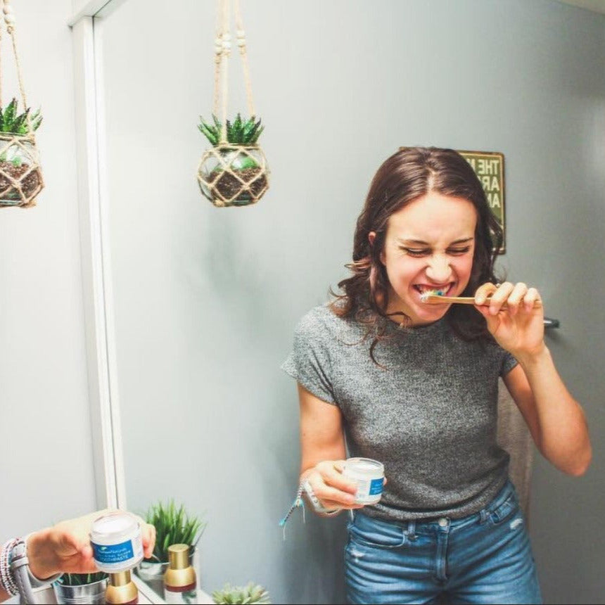 Woman using Nelson Naturals Spearmint Toothpaste in a Jar with bamboo toothbrush in a modern bathroom