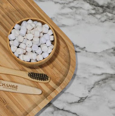 Canadian made Change Toothpaste tablets in a wooden dish with two Change Toothpaste bamboo toothbrushes on bamboo tray