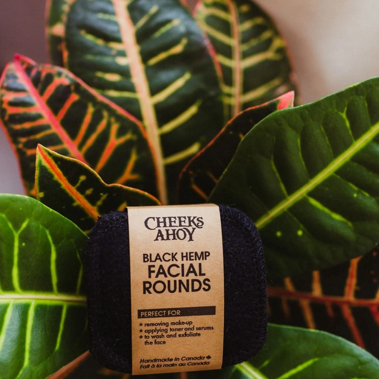 Set of 6 black reusable hemp facial rounds by Cheeks Ahoy with label sitting in a plant with big leaves.