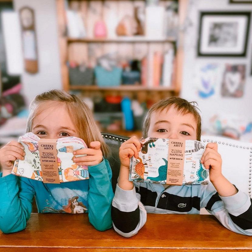 A boy and girl holding up reusable cloth napkins for children that are handmade in Canada by Cheeks ahoy and available in sets of 10.