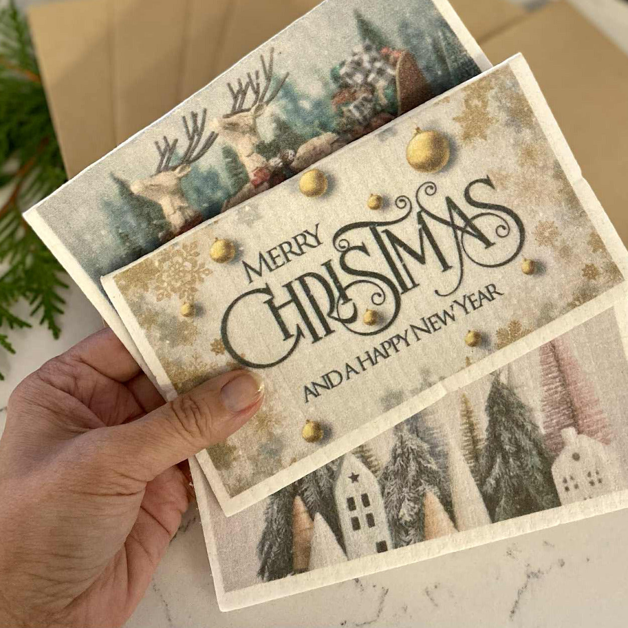 Hand holding Swedish dishcloth Christmas cards with festive eco-friendly designs – reusable, compostable, sustainable holiday greeting cards with envelopes by Earthly Change.