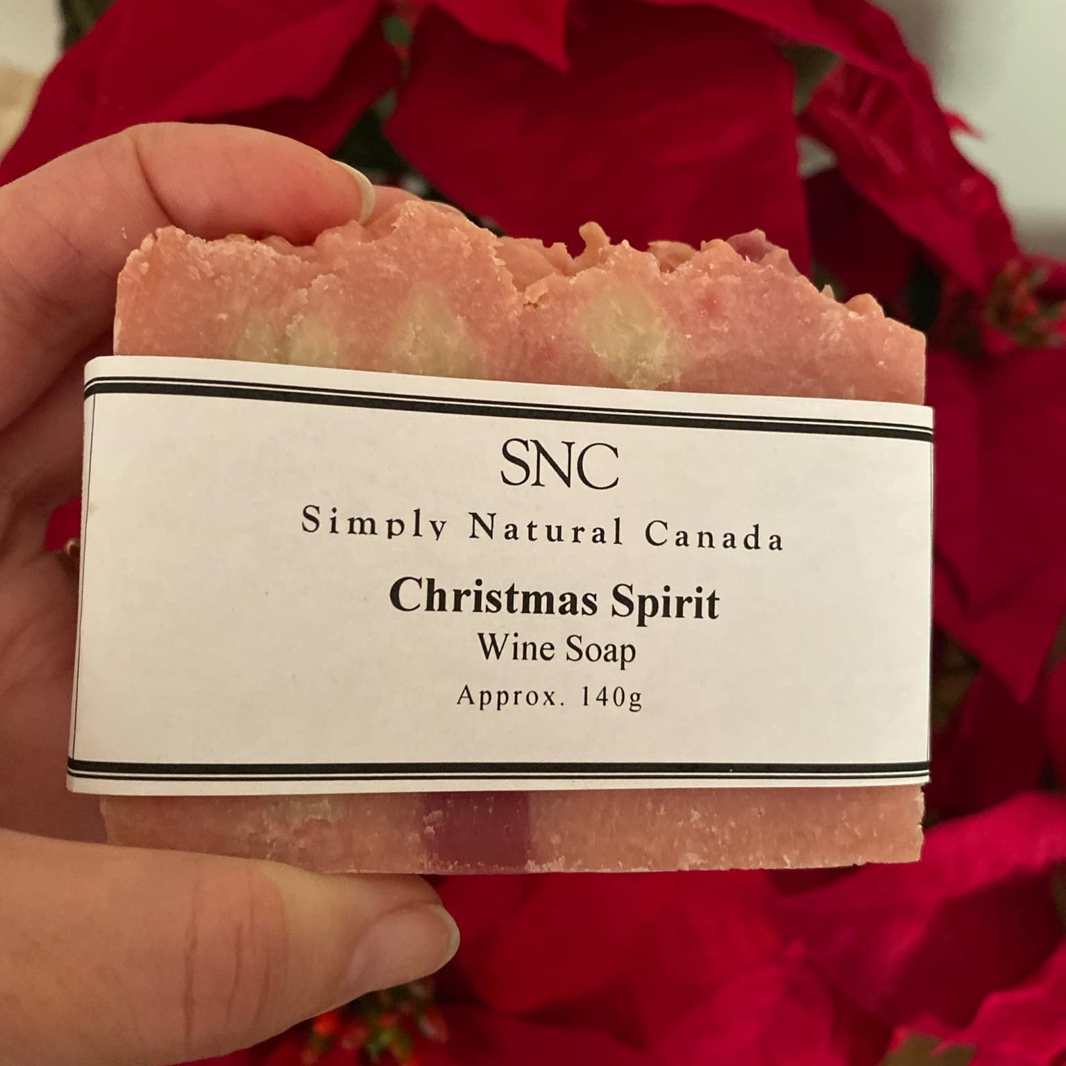 Our black and white labeled Christmas Spirit Wine Soap 140 g approx. is shown in front of a poinsettia plant.