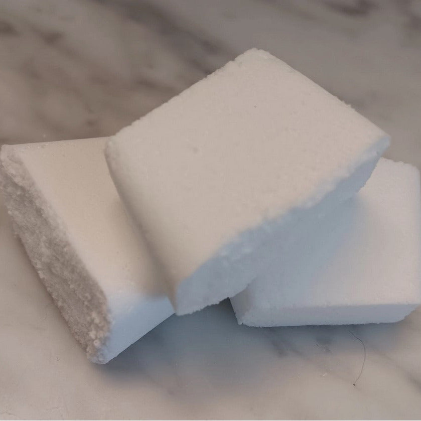 Close-up of Earthly Change natural toilet cleaning tablets made with non-toxic ingredients, showing their solid white texture on a marble surface.