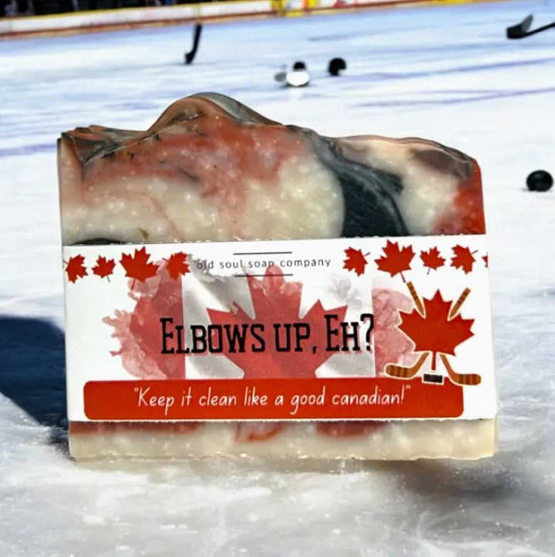 Elbows Up, Eh? Canadian bar soap by Old Soul Soap Company on outdoor hockey rink, featuring red, black, and white swirls with maple leaf-themed label.