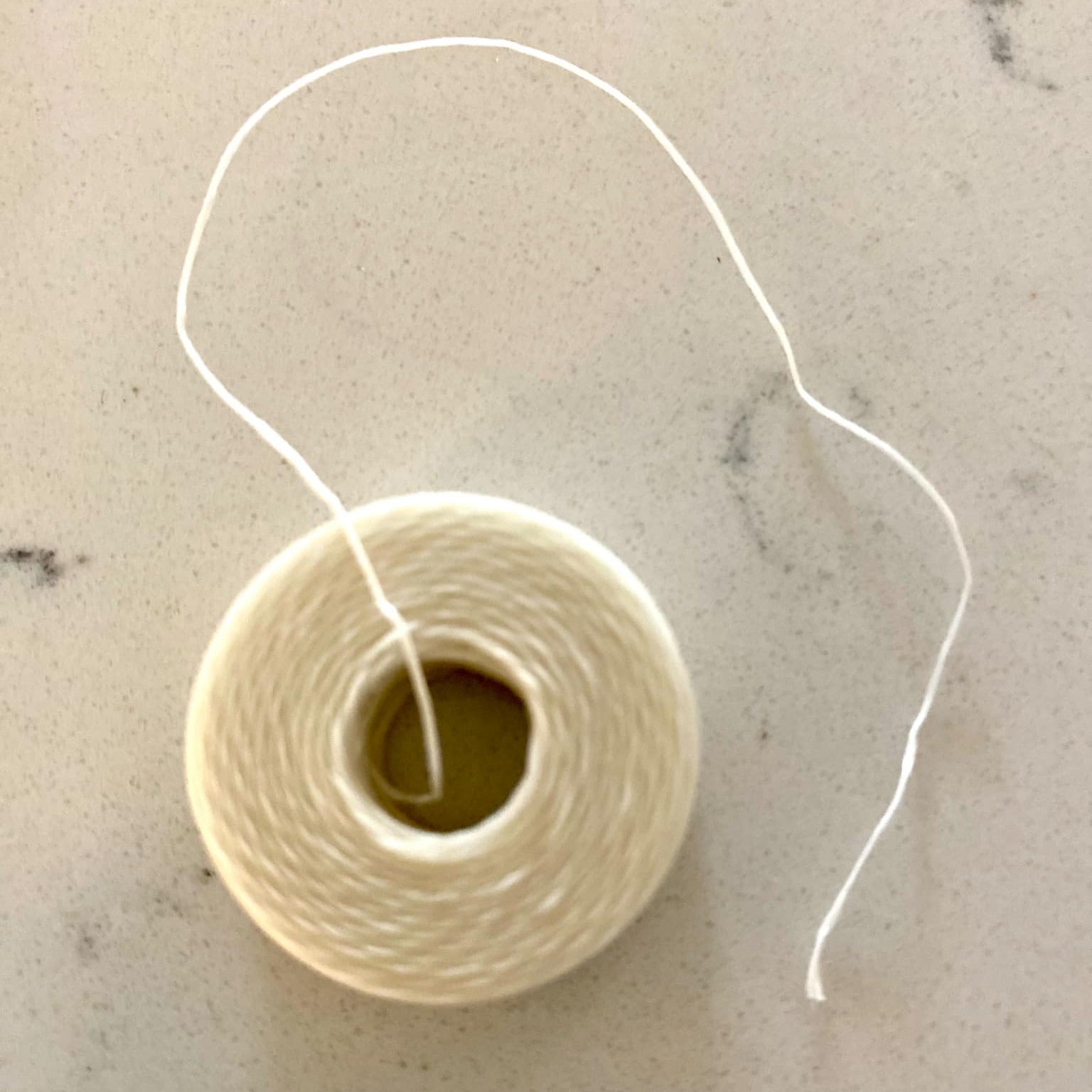 Spool of white dental floss on a marble surface