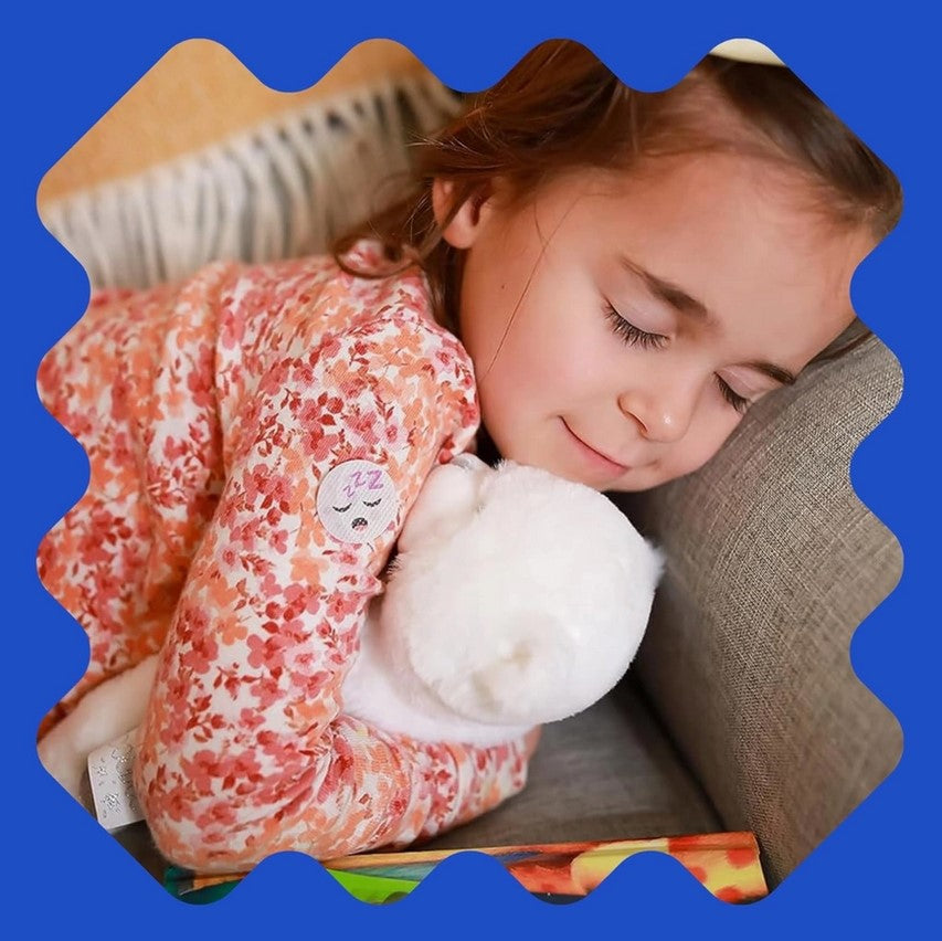 Child in a patterned outfit holding a white fluffy toy, sitting on a couch with a blue border.