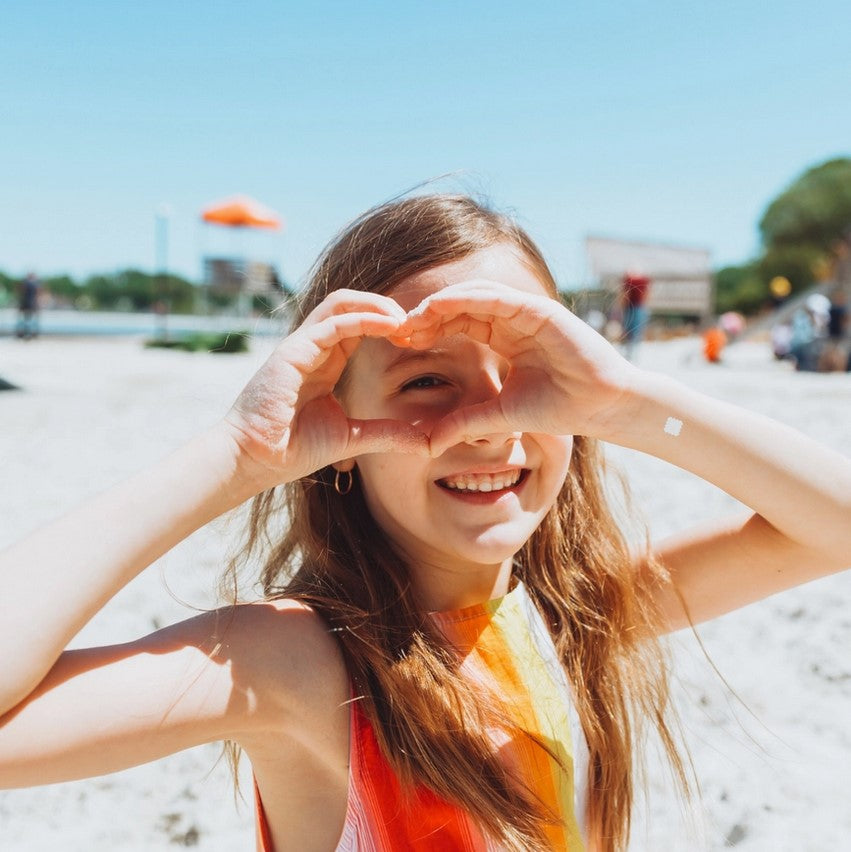 Young girl making a heart shape with her hands on a beach