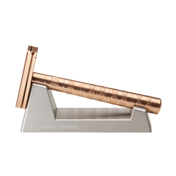 Copper Henson Razor angled in durable anodized aluminum razor stand