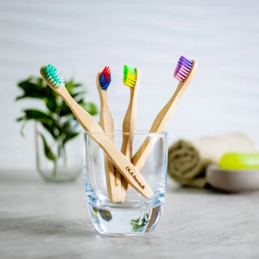 Canadian-made OLA Bamboo Toothbrush Set of 4 for children - the toothbrushes teal/white, red/blue, yellow/green and pink/purple sit in a clear glass