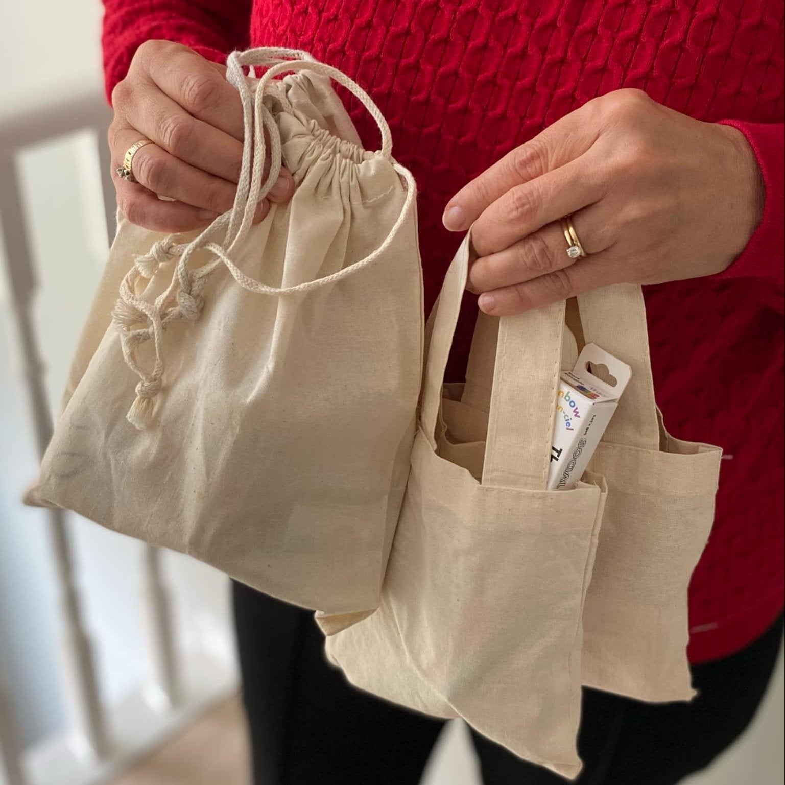 Woman holding 4 sizes of Simply Natural Canada reusable cotton bags filled with a variety of sustainable personal care and household cleaning products available while supplies last.
