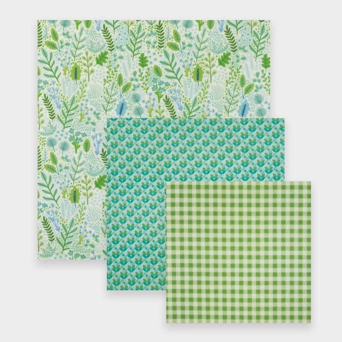 A set of three beeswax food wraps in green and floral patterns, presented in different sizes.