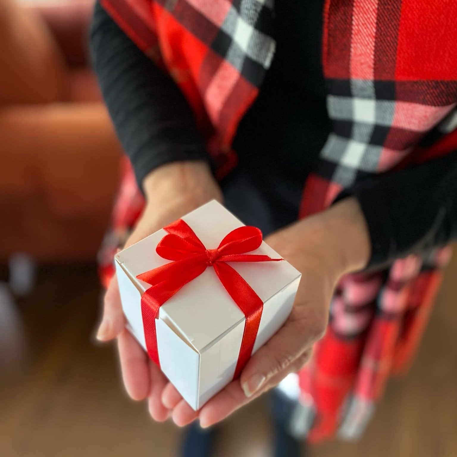 5 handmade eucalyptus mint shower steamer in a white square gift box with a red ribbon in the hands of a woman wearing a red, black and white plaid scarf.