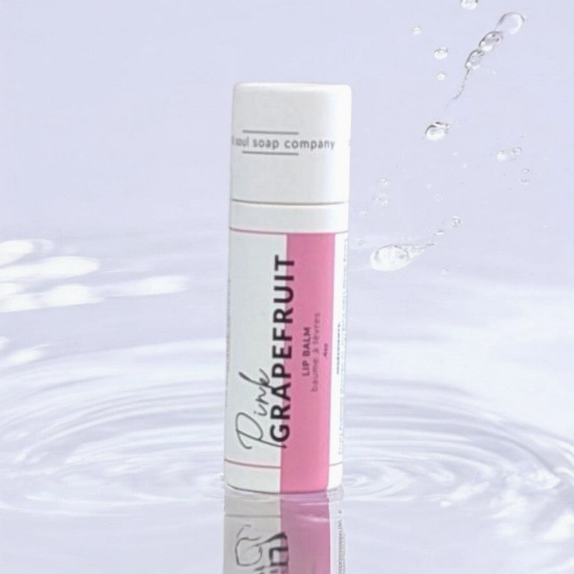 Close-up of the pink grapefruit-colored balm tube cap with textured finish and clear branding label in soft natural light