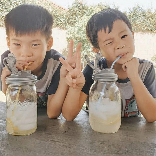 Two children drinking lemonade with straws from Mason jars using reCAP POUR lids – eco-friendly reusable drink containers for kids