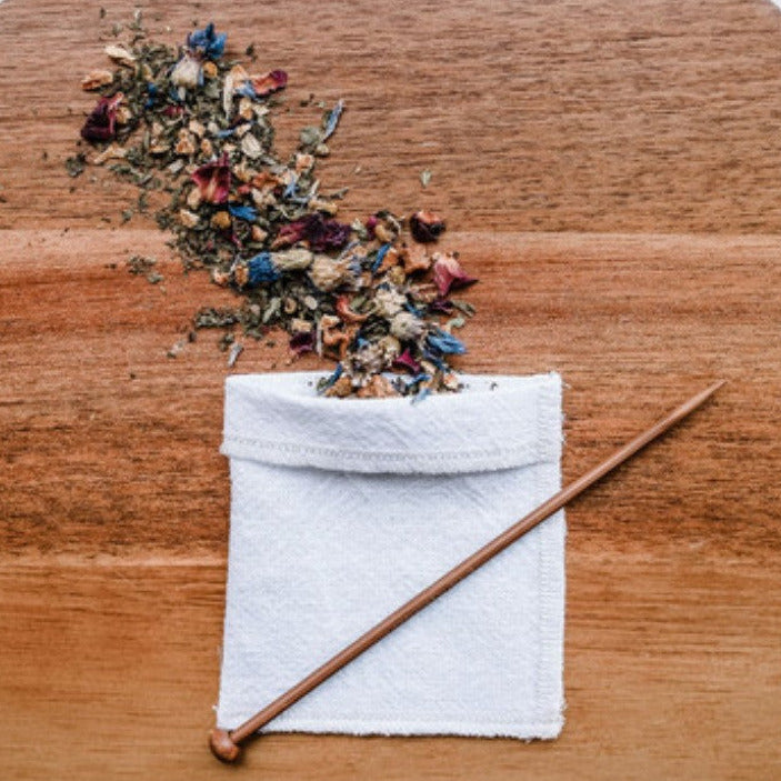 Eco-friendly reusable tea bag made from 100% organic cotton with wooden balancing stick and loose leaf tea on wooden board – sustainable zero-waste tea accessory.