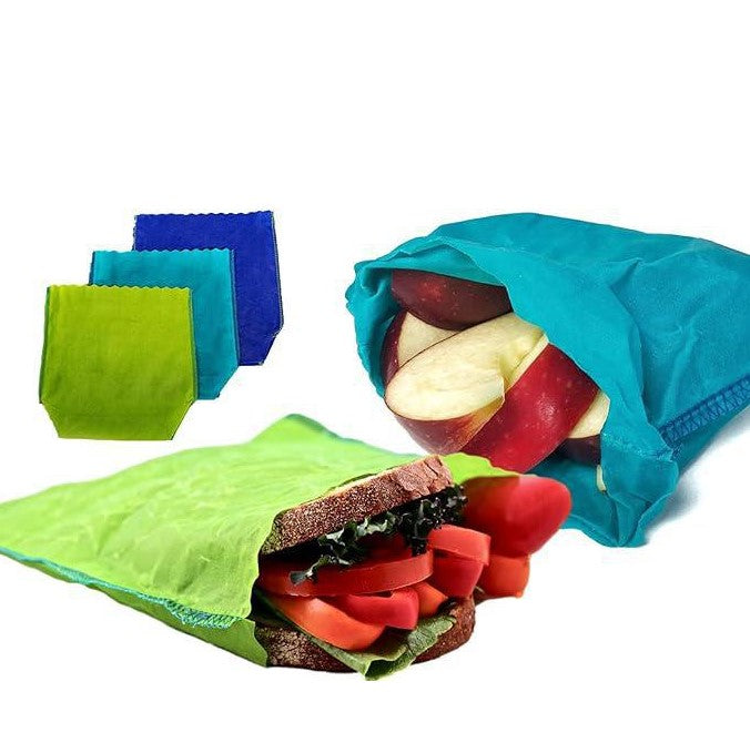 Beeswax sandwich bags made in Canada by etee are shown on a white background. On the left side the three available colors - lime green, teal and blue are displayed and in the forefront a sandwich is packaged in a lime green bag while a teal bag has some cut apple pieces coming out of it.