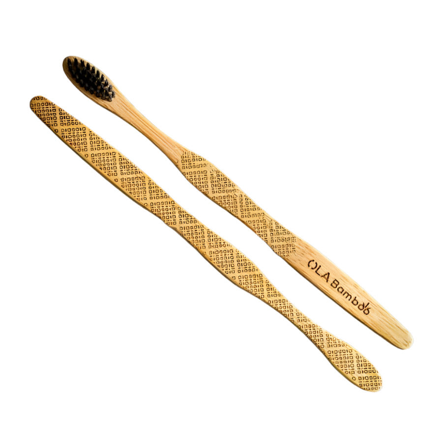 Canadian-made OLA Bamboo toothbrush with charcoal bristles is shown out of the box - one toothbrush is shown with bristles up and other is of the bristle head face down to demonstrate what the pattern on the back of the toothbrush looks like.