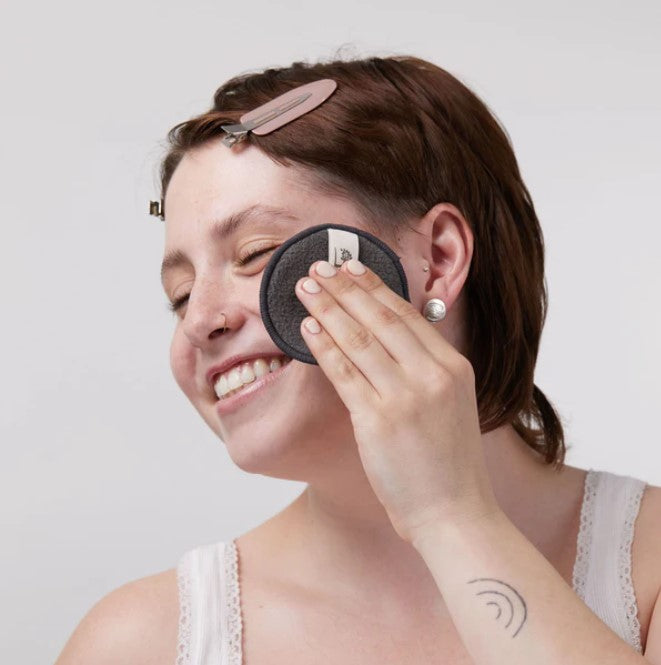 Woman using a single reusable bamboo charcoal facial round on her face to remove make up and/or apply facial toner.