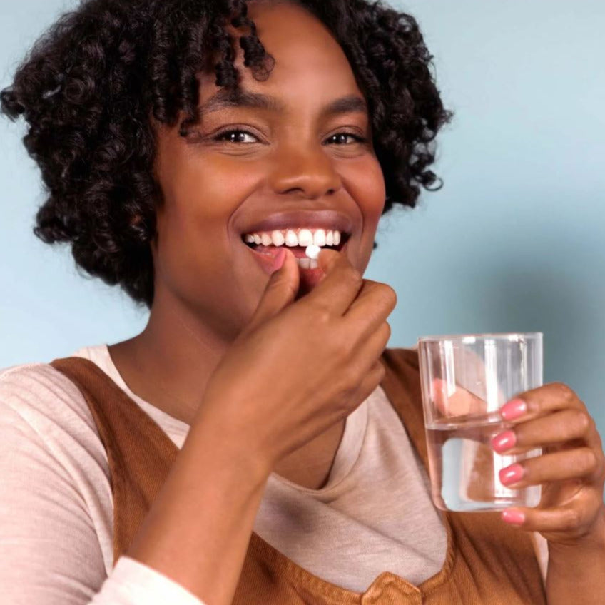 Woman using a Canadian made TANIT mouthwash tablet with glass of water – plastic-free oral care alternative