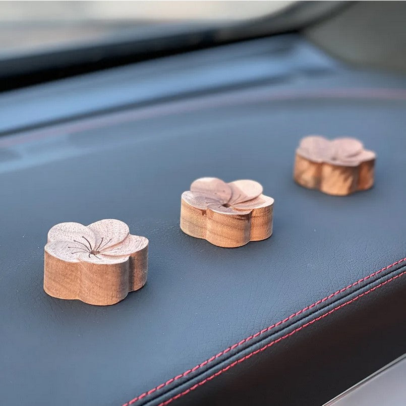 three wooden essential oil diffusers in a flower shape lined up on a car dash are sold individually with or without clips to attach them to the car vents