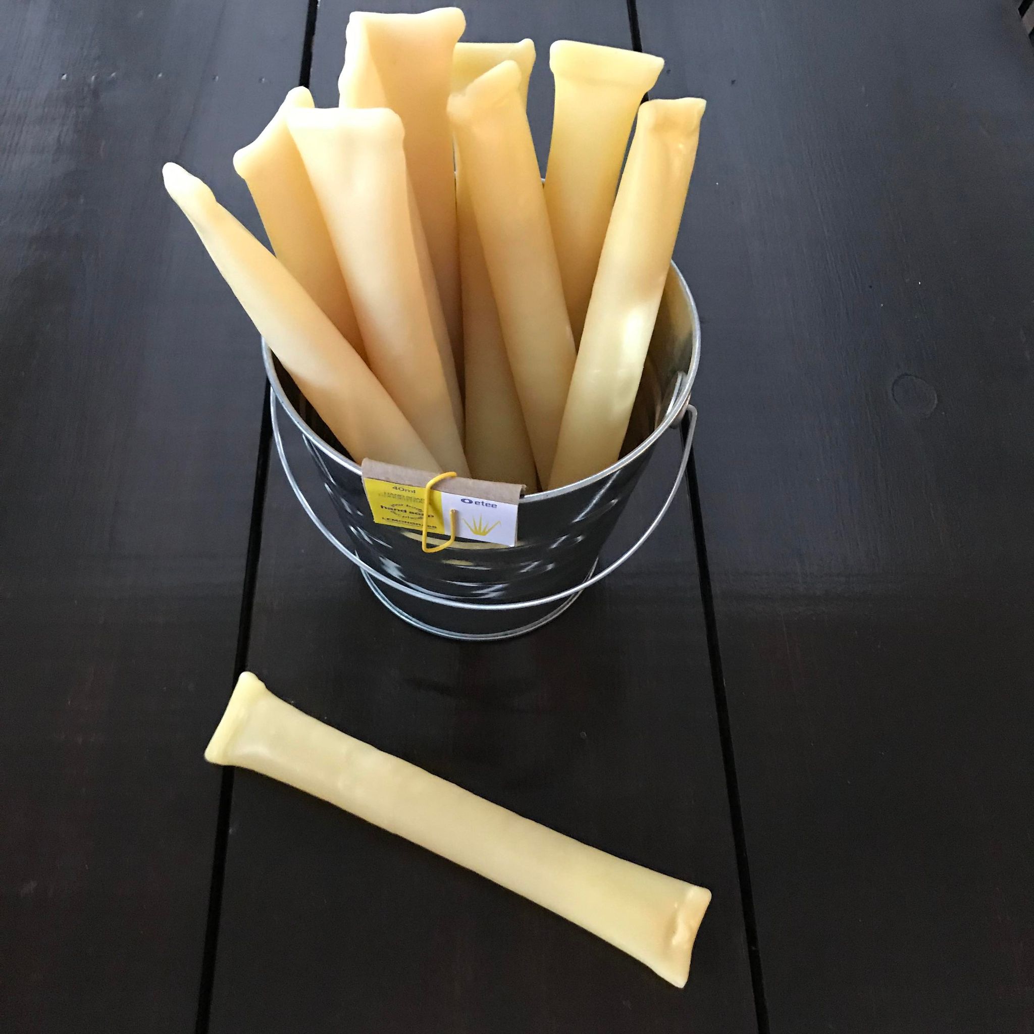 Dish soap concentrate in lemongrass essential oil scent packaged in a compostable beeswax pods shown in an aluminum pail with a single pod in front. This dish soap concentrate is make in Canada by etee and is sold both individually as well as in packs of three