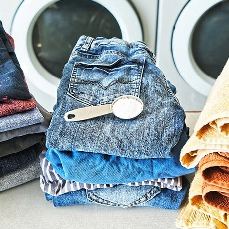 A tsp of etee's concentrated powdered laundry detergent sits on a pile of clean folded laundry