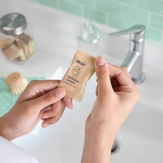 A woman hold a bathroom spray cleaner tablet in a pouch by Nature Bee Goods 
