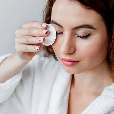 A white sustainable LastRound makeup remover pad being used by a woman to remove her eye makeup