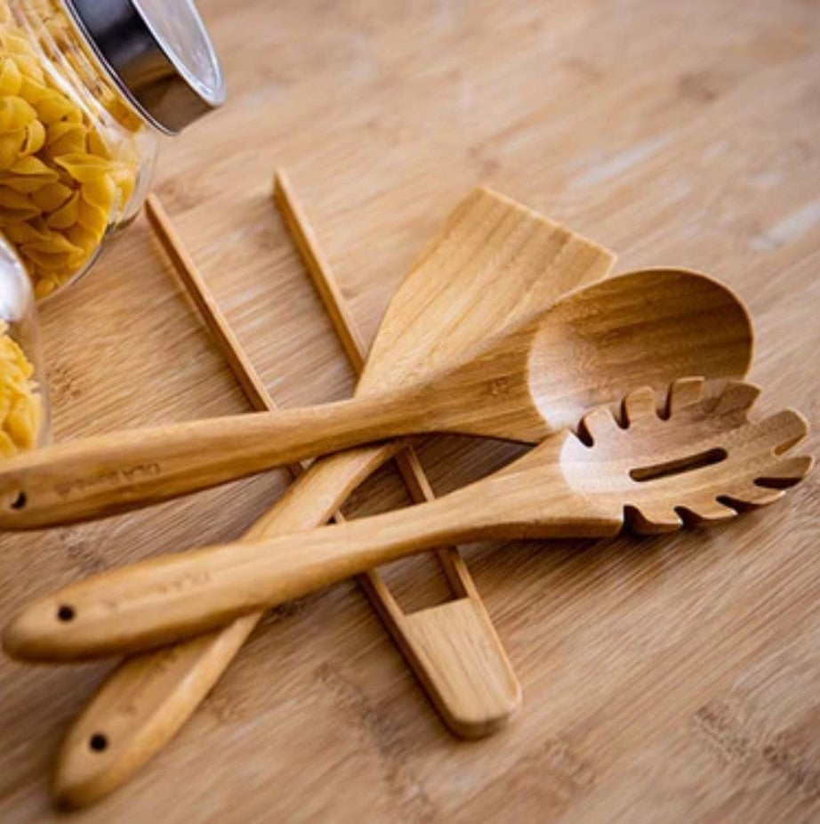 Ola Bamboo eco-friendly cooking utensils laid flat on bamboo surface with pasta jar in the background