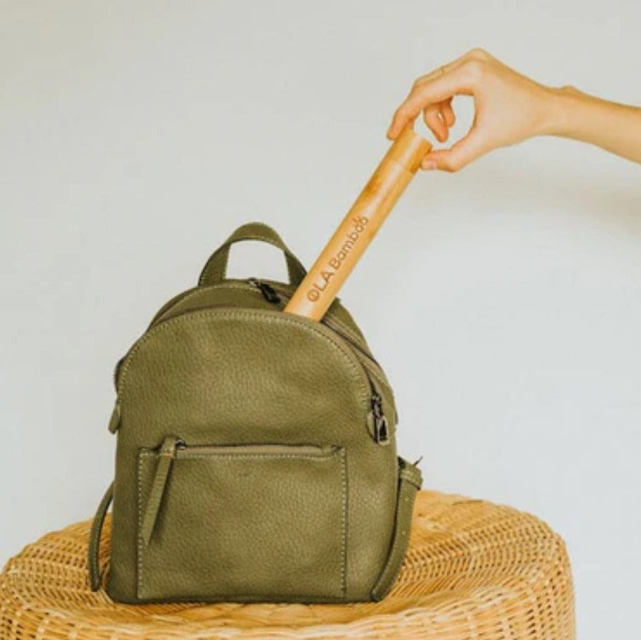 Hand placing Ola Bamboo toothbrush travel case into green backpack