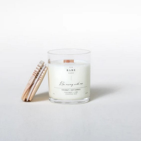 This 'Run away with me' coconut and soy candle scented with bergamot and lime essential oils is made in Canada by The Bare Home and features a wooden wick and a wooden lid. It is pictured on a white background with the lid off.