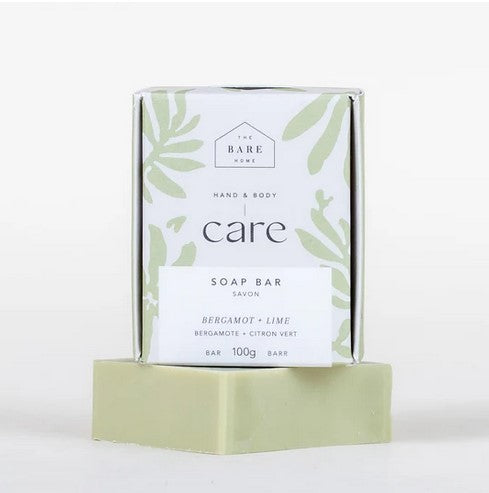 The 100 g light green bergamot lime hand and body bar soap is pictured on a white background with the soap bar box on top of it in white and light green. 