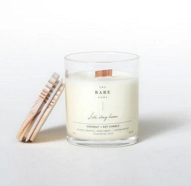 This 'Let's stay home' coconut and soy candle scented with blood orange, bergamot and sandalwood essential oils is made in Canada by The Bare Home and features a wooden wick and a wooden lid. It is pictured on a white background with the lid off.