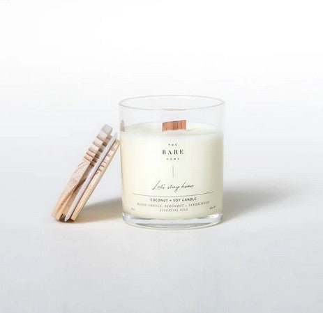 This 'Let's stay home' coconut and soy candle scented with blood orange, bergamot and sandalwood essential oils is made in Canada by The Bare Home and features a wooden wick and a wooden lid. It is pictured on a white background with the lid off.