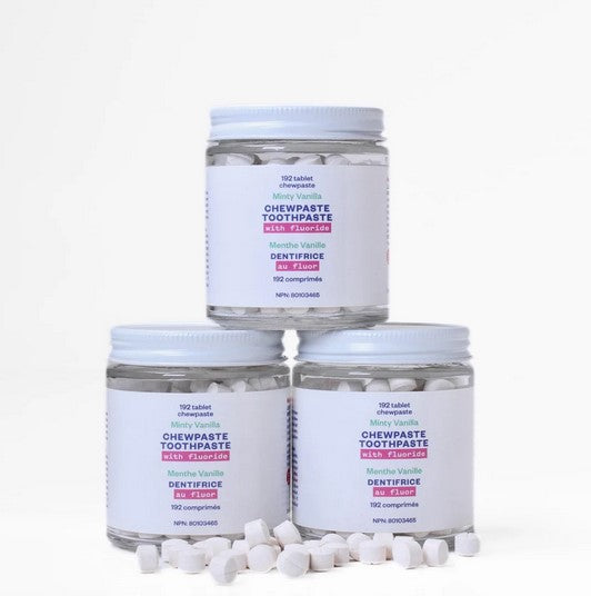 Three glass jars of fluoride chewpaste toothpaste tablets by etee stacked with tablets scattered in front – plastic-free packaging