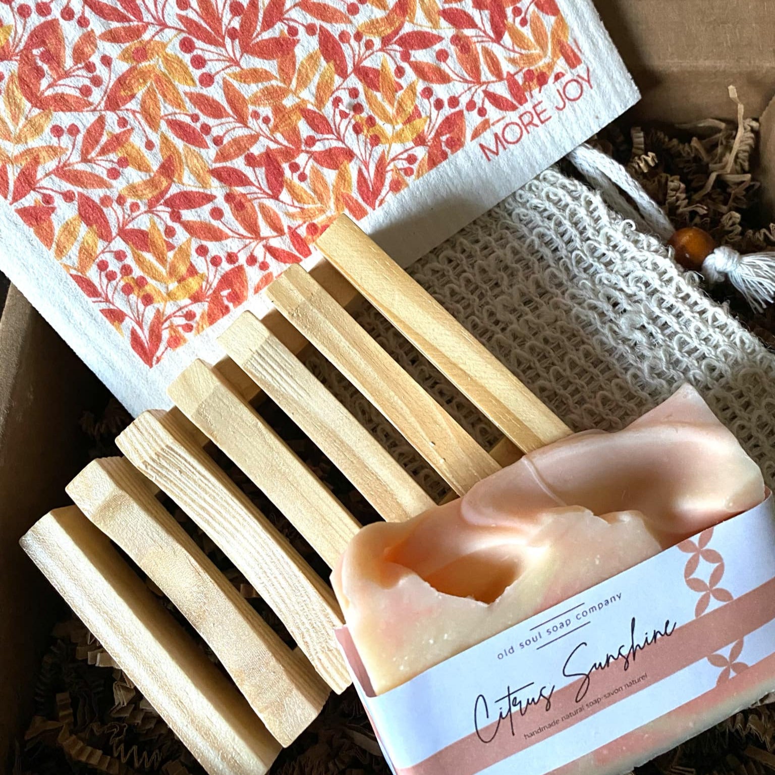 Bar of soap with a decorative label on a wooden soap dish, with a patterned towel in the background.