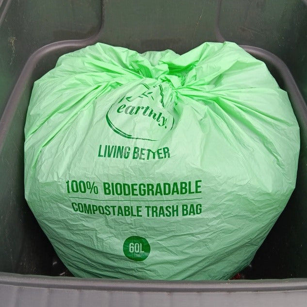 Earthly 60L compostable garbage bag tied and placed in large outdoor bin, labeled 100% biodegradable compostable trash bag