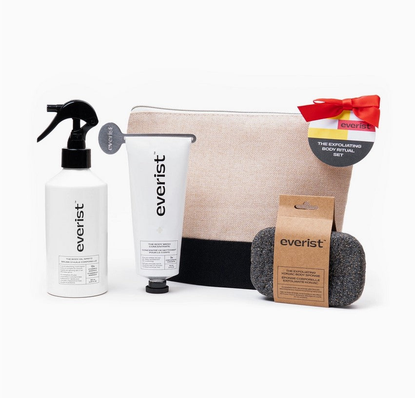 A full-size Exfoliating Body Wash Concentrate, Body Oil Spritz, Exfoliating Konjac Body Sponge sit in front of a  Black Jute Travel Bag on a white background. 
