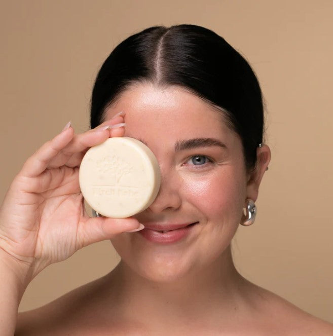 Female model holding a Canadian made round vegan facial bar made with oatmeal for gently cleansing your skin by Birch Babe