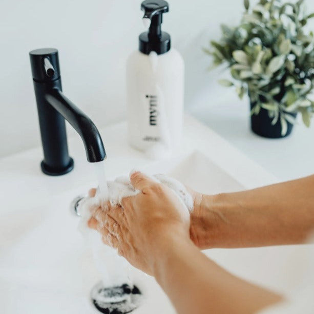 Hands being lathered up in a bathoom sink with Canadian made foaming hand soap from a black and white wheat straw myni foamer pump dispenser