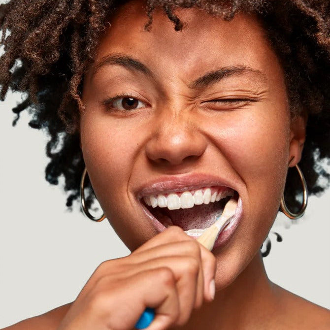 Woman brushing her teeth with a bamboo toothbrush and natural toothpaste, promoting eco-friendly and fluoride-free oral care from Nelson Naturals.