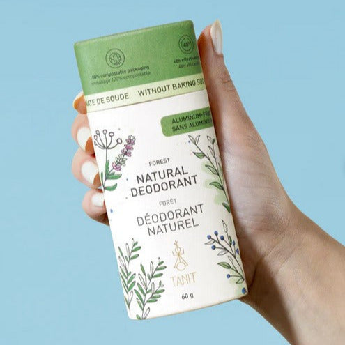 Hand holding a compostable cardboard tube of Canadian made essential oil scented natural deodorant with a blue background