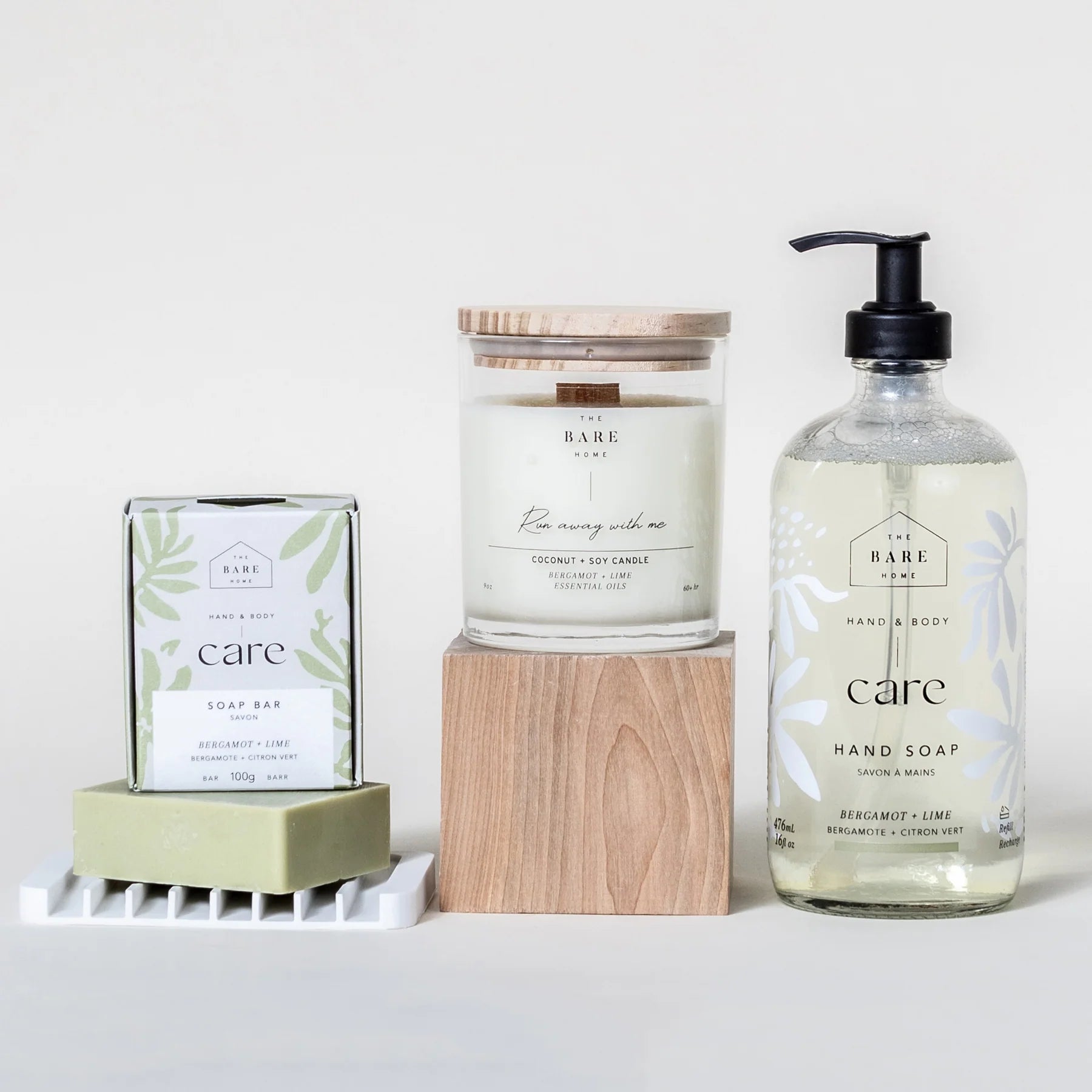 The Bare Home's Care Kit in Bergamot Lime is pictured on a white background. It is all natural, eco-friendly and includes a liquid hand soap in a 476ml glass pump bottle, a 100g body bar, candle in a glass jar and white silicone soap dish.