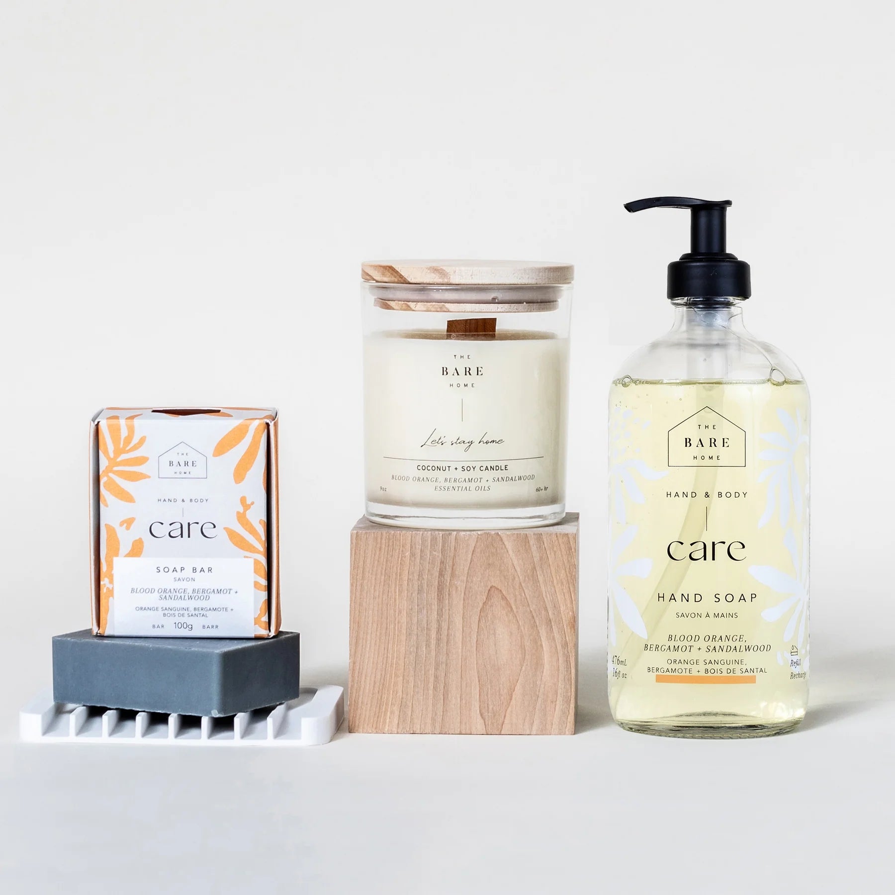 The Bare Home's Care Kit in Blood Orange, Bergamot and Sandalwood is pictured on a white background. It is all natural, eco-friendly and includes a liquid hand soap in a 476ml glass pump bottle, a 100g body bar, candle in a glass jar and white silicone soap dish.